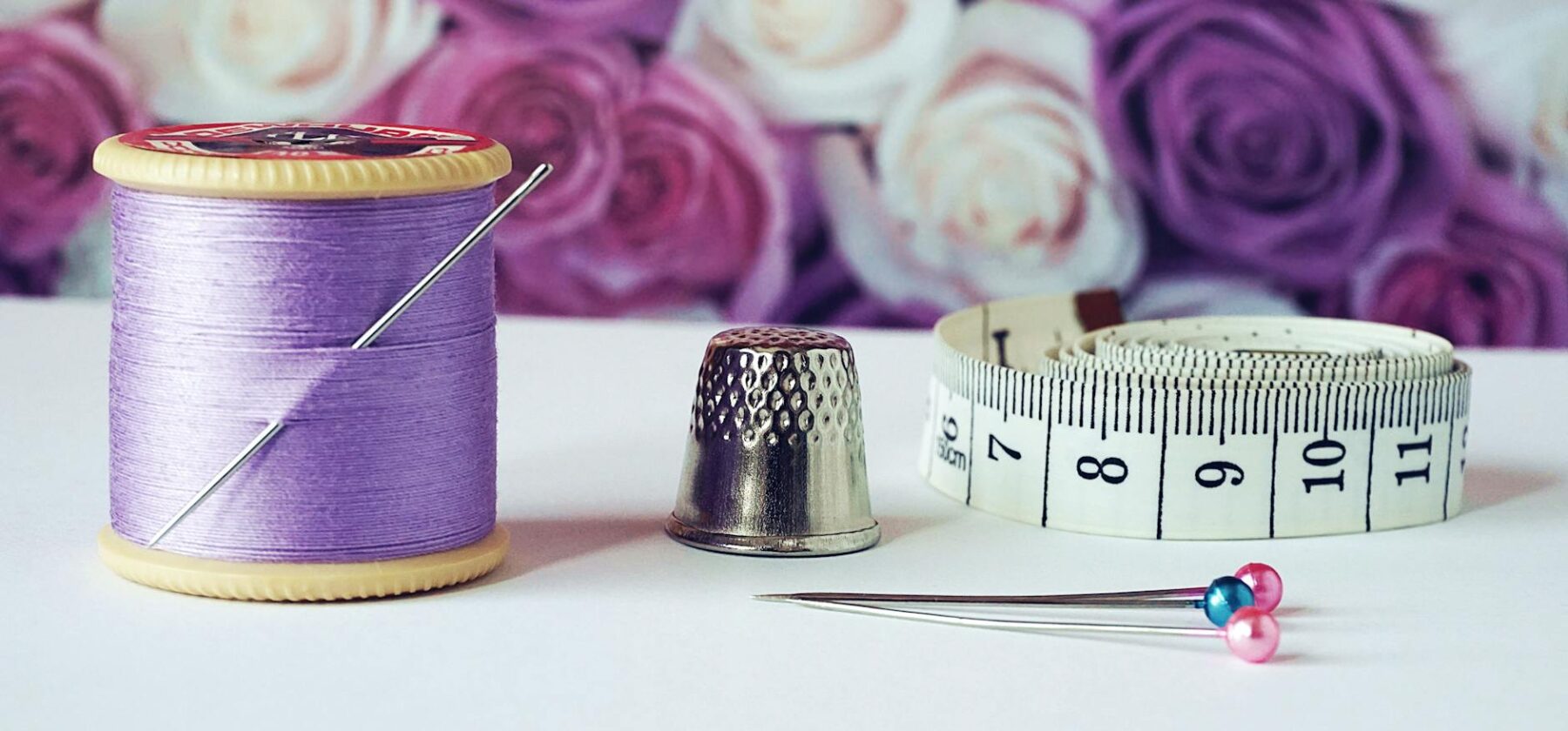 spool of purple thread near needle thimble and measuring tape